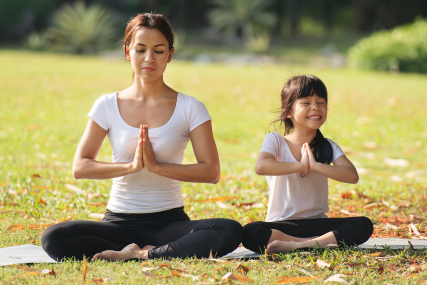 Mother daughter sitting in a park on yoga mats.