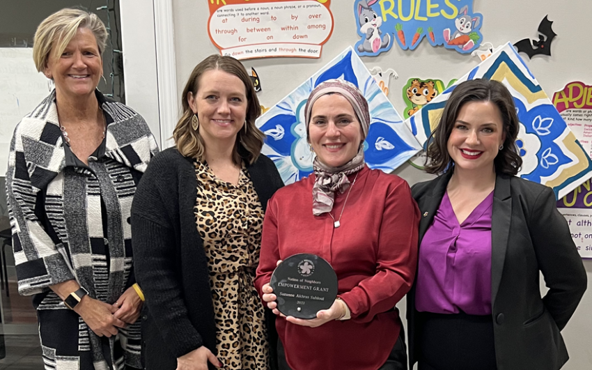 Four smiling women, one with an award.