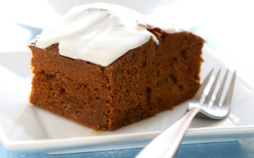 Gingerbread with cream cheese frosting on a white plate with a fork on a blue snowflake tablecloth.