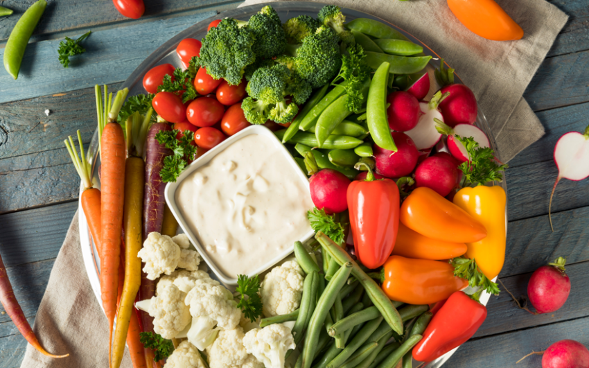 Colorful veggie plate with dip on a rustic blue-gray wooden table.