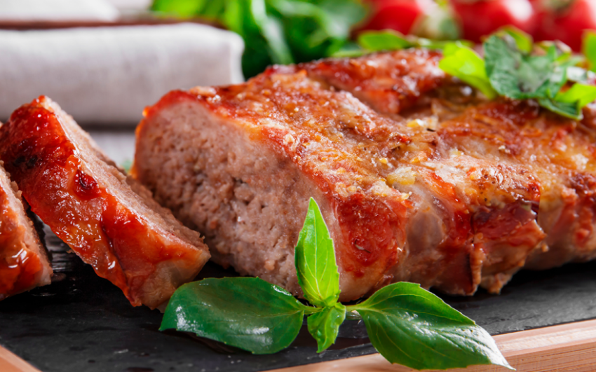 Close up of a meatloaf cut on a plate with green leaves.