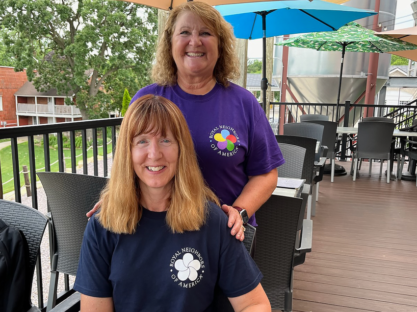 Two smiling women on a patio wearing Royal Neighbors t-shirts.