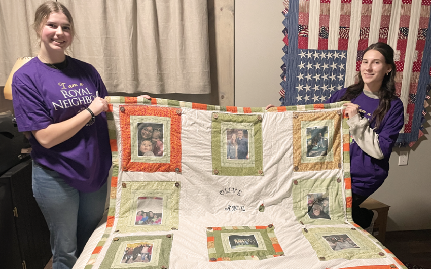 Two smiling girls holding a quilt.