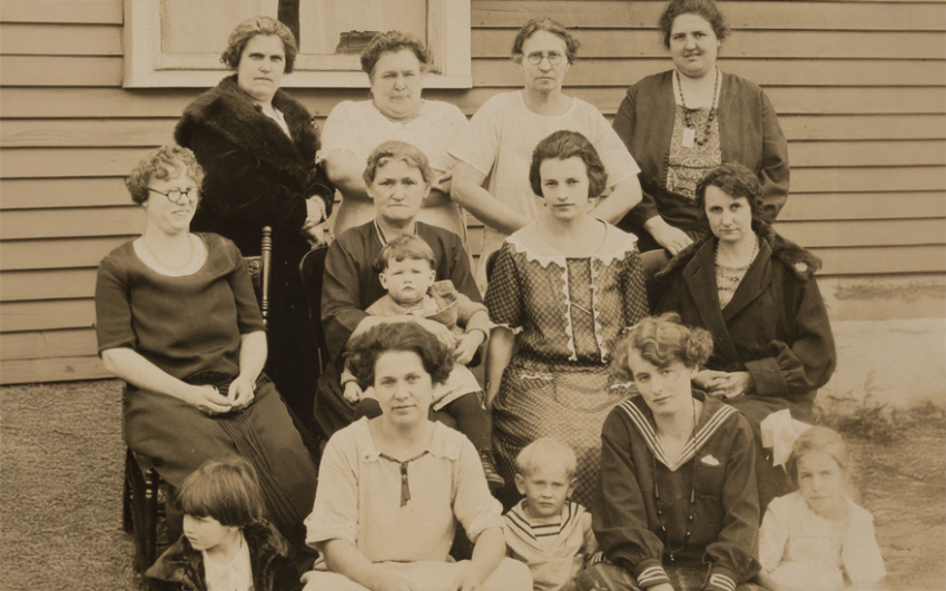 Old lack and white photo of woman and children outside in front of a house.