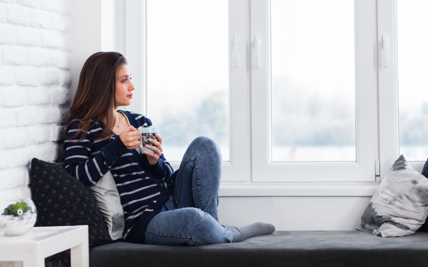 Young woman holding coffee, relaxing in a big white window.