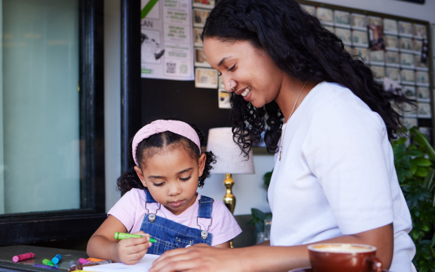 Smiling mother with daughter coloring at a counter in a coffee shop.