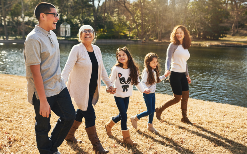 Happy multigenerational family holding hands and walking by water outside in the sunshine.