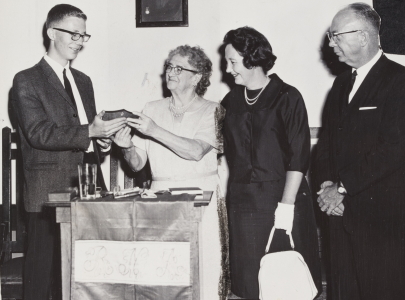 Black and white photo of a young man student accepting a scholarship with three adults.